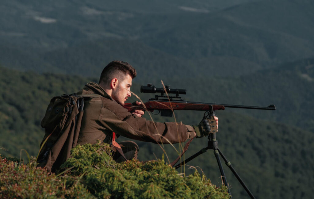 Precisión en Cada Disparo: Encuentra tu Visor Ideal Cazador con rifle y visor apuntando a distancia en campo abierto, simbolizando precisión y armonía con la naturaleza.