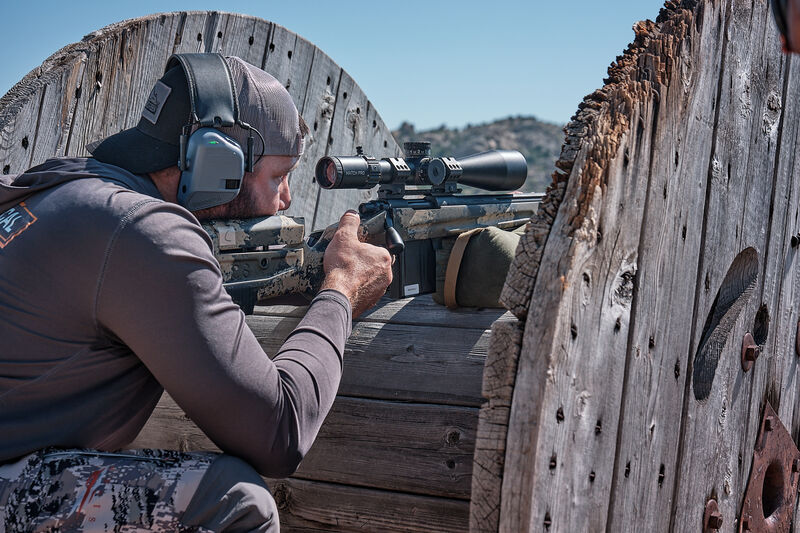Tirador apuntando con un Visor Bushnell Match Pro ED instalado en un rifle. El tirador está apostado en una bobina de madera de hilo de cobre.